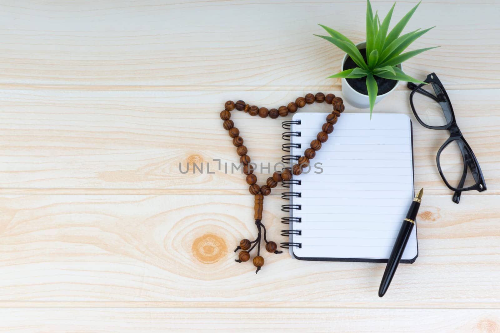 Flat lay view of workspace with Pen, spectacles, decoration flower, rosary and book. Copy Space, business and education concept.