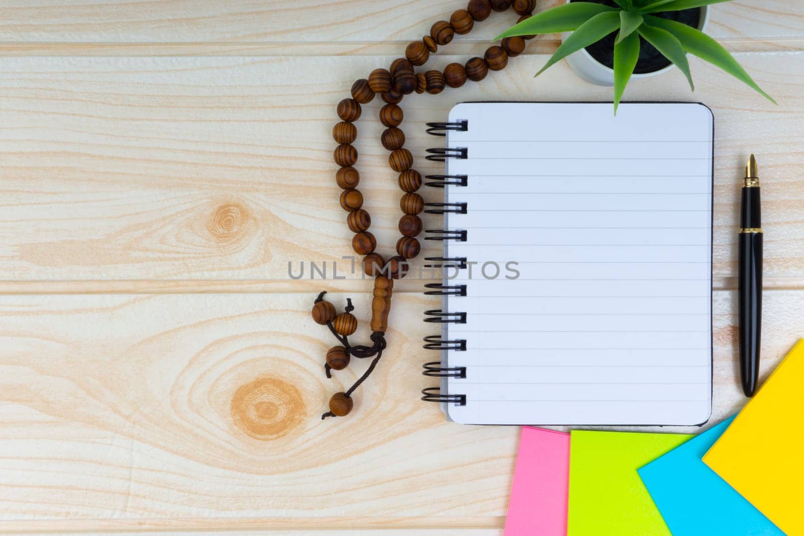 Flat lay view of workspace with Pen, spectacles, decoration flower, rosary and book.Copy Space, business and education concept.