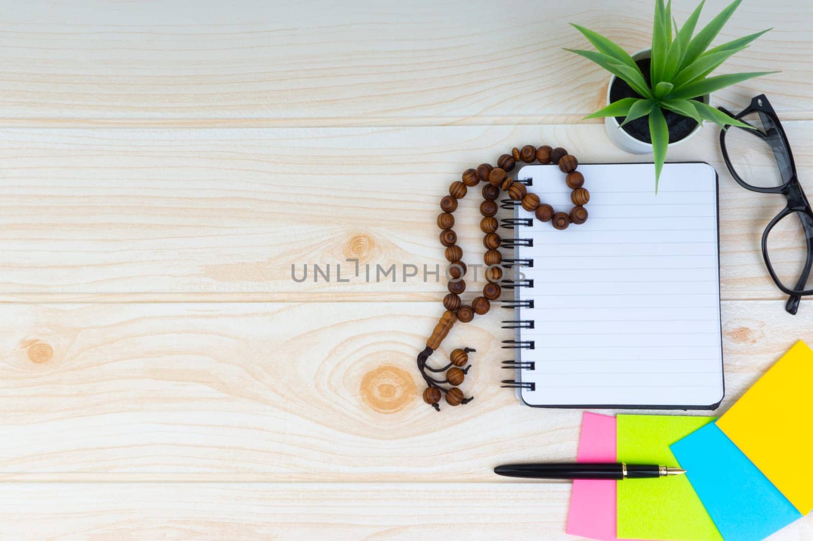 Flat lay view of workspace with Pen, spectacles, decoration flower, rosary and book.Copy Space, business and education concept.