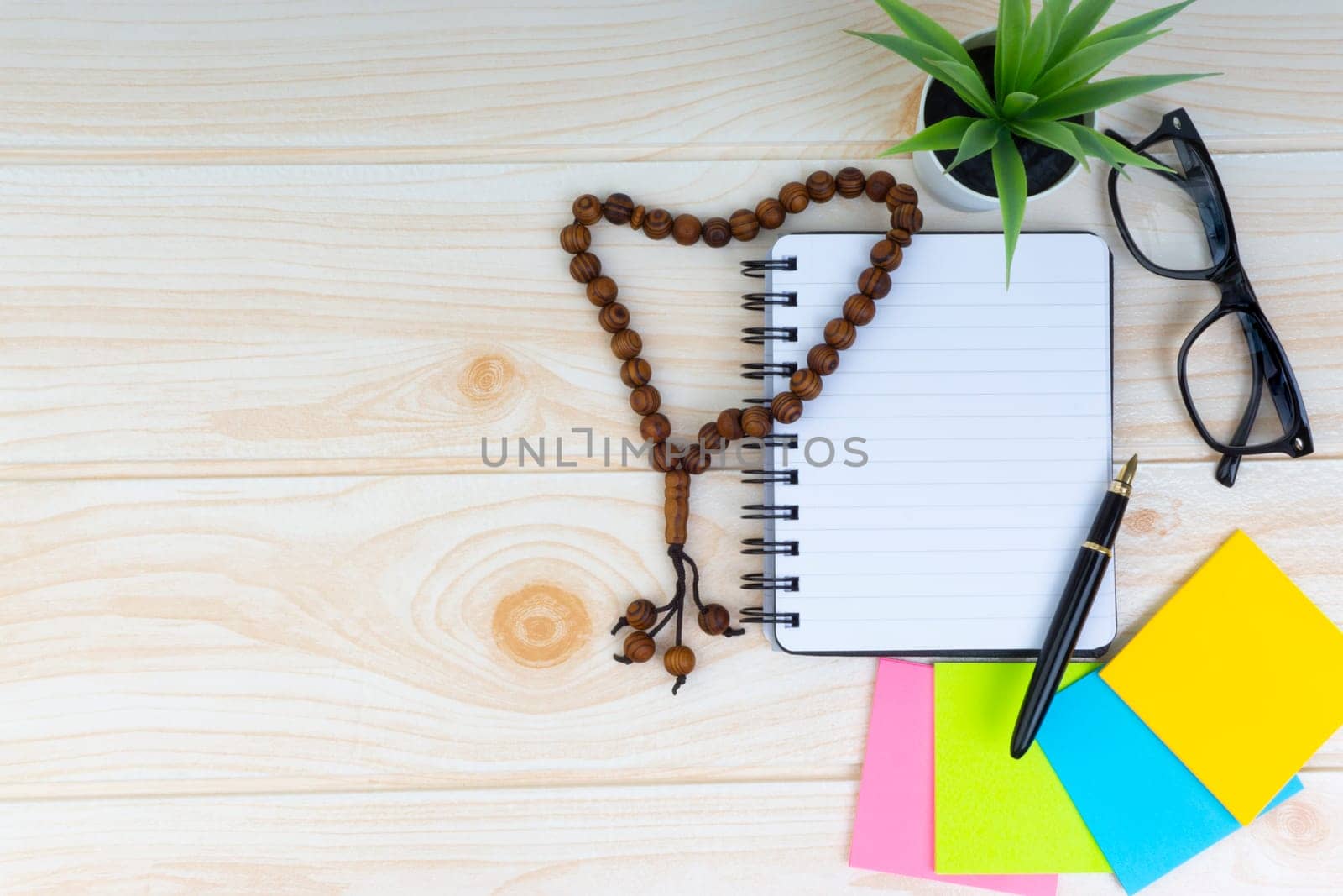 Flat lay view of workspace with Pen, spectacles, decoration flower, rosary and book.Copy Space, business and education concept.