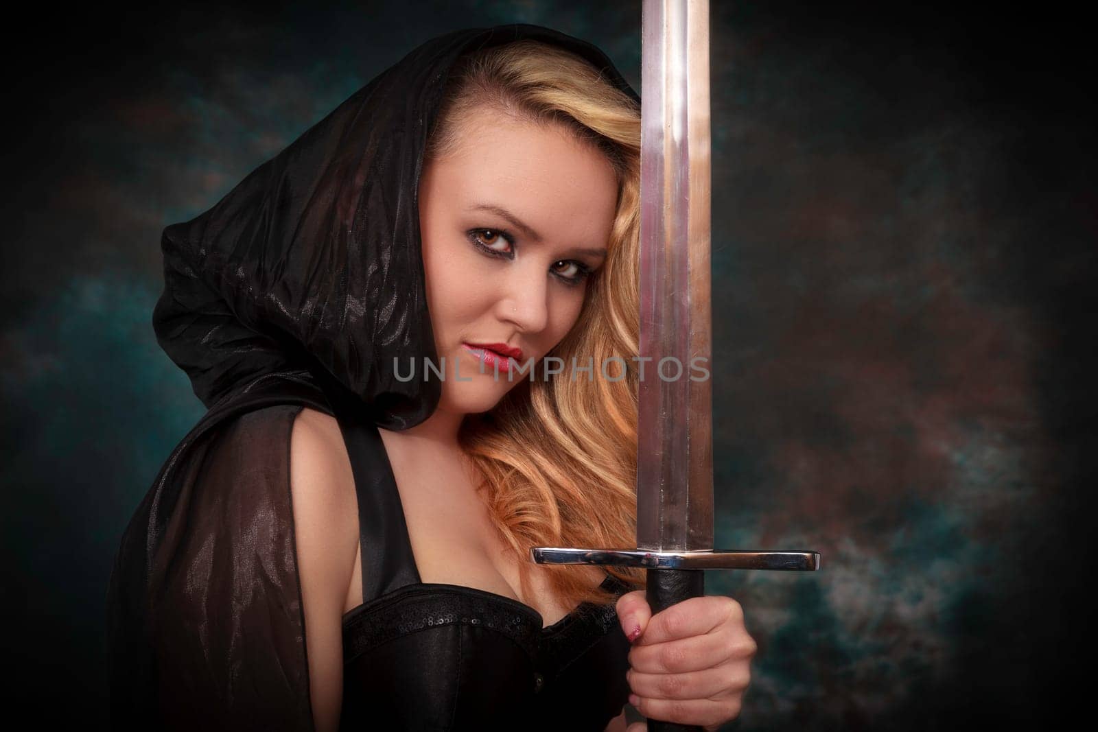 young beautiful woman with a sword in the hand in black cape. Amazon woman.