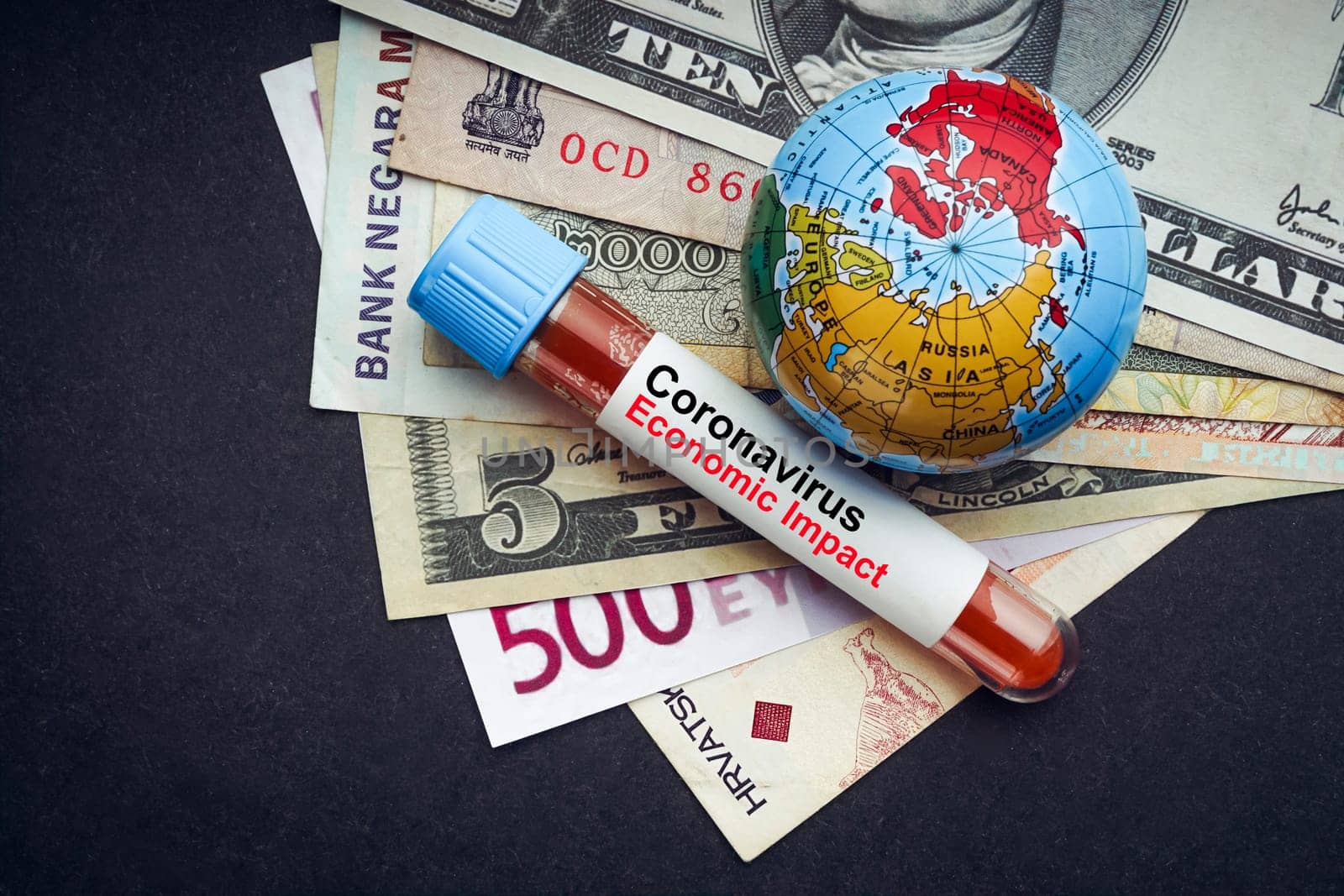 CORONAVIRUS ECONOMIC IMPACT text with currency banknotes, world globe and blood test vacuum tube on black background. Covid-19 or Coronavirus Concept