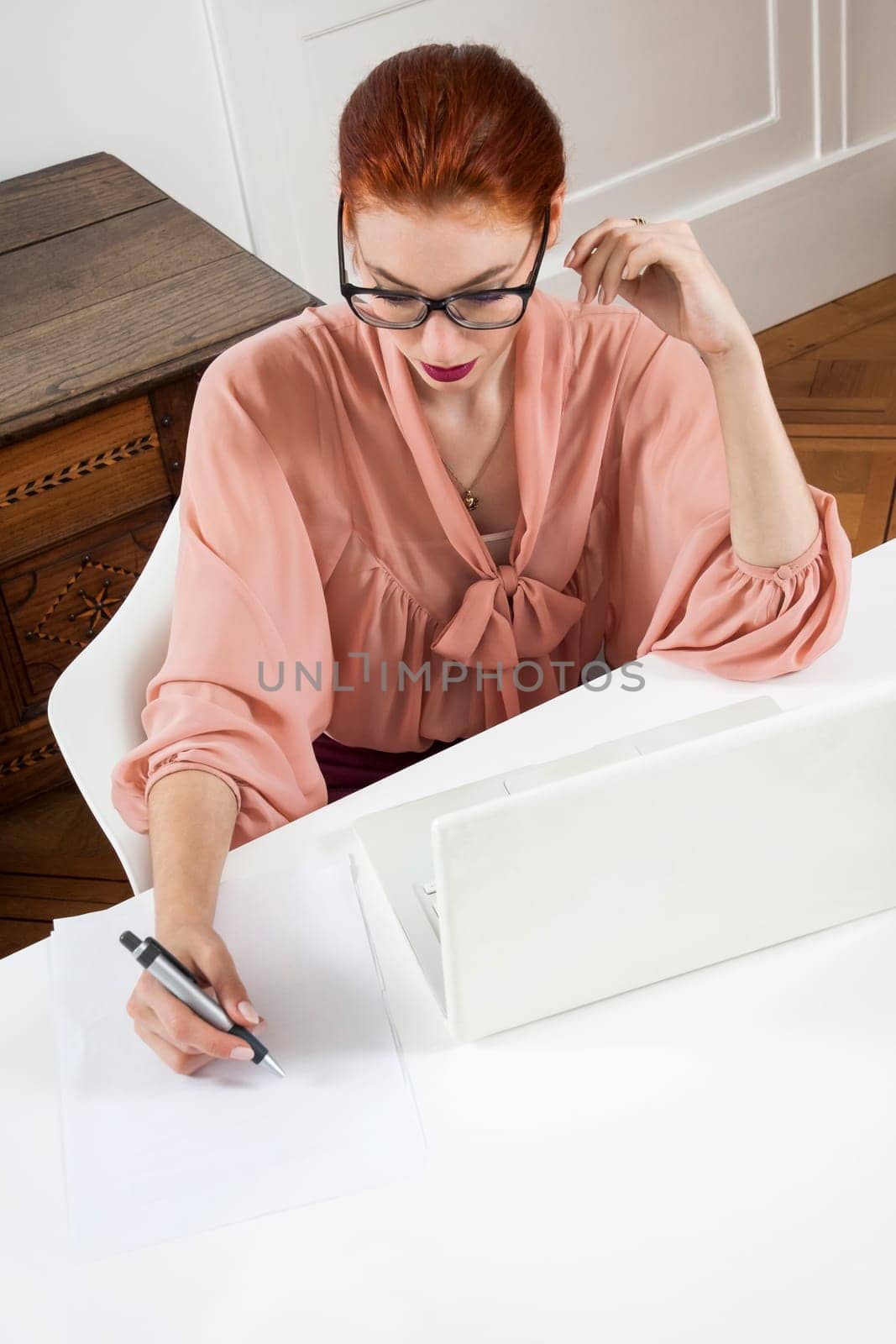 Young businesswoman reads statistics at the desk on the computer with red hair and glasses in the office