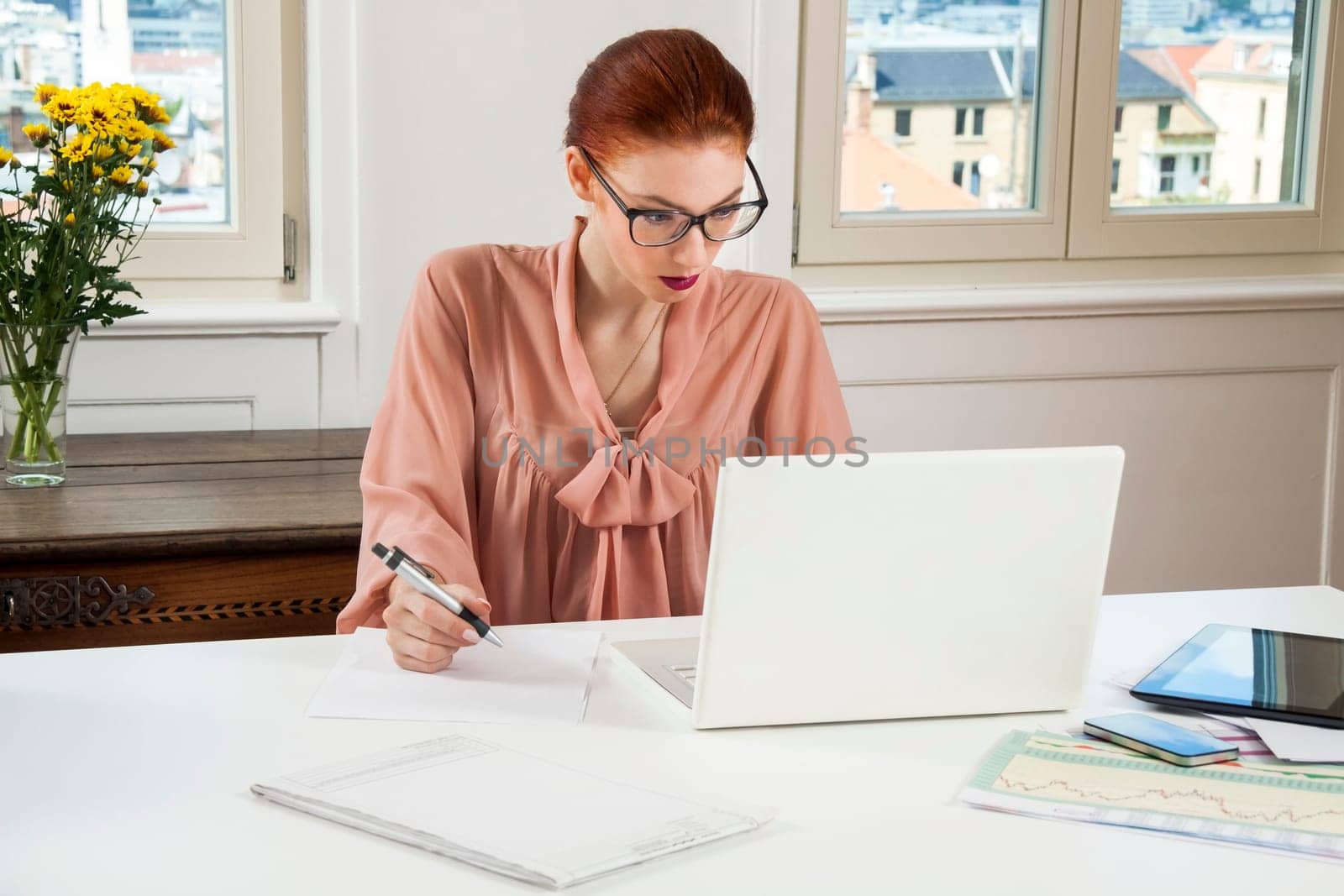 Young businesswoman reads statistics at the desk on the computer with red hair and glasses in the office
