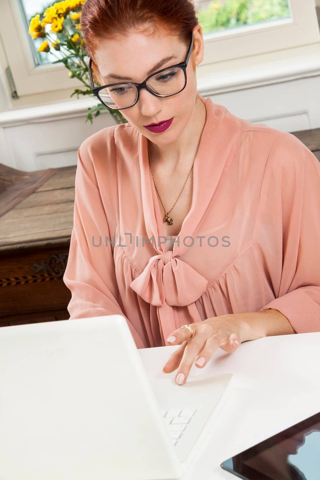 Young businesswoman reads statistics at the desk on the computer with red hair and glasses in the office