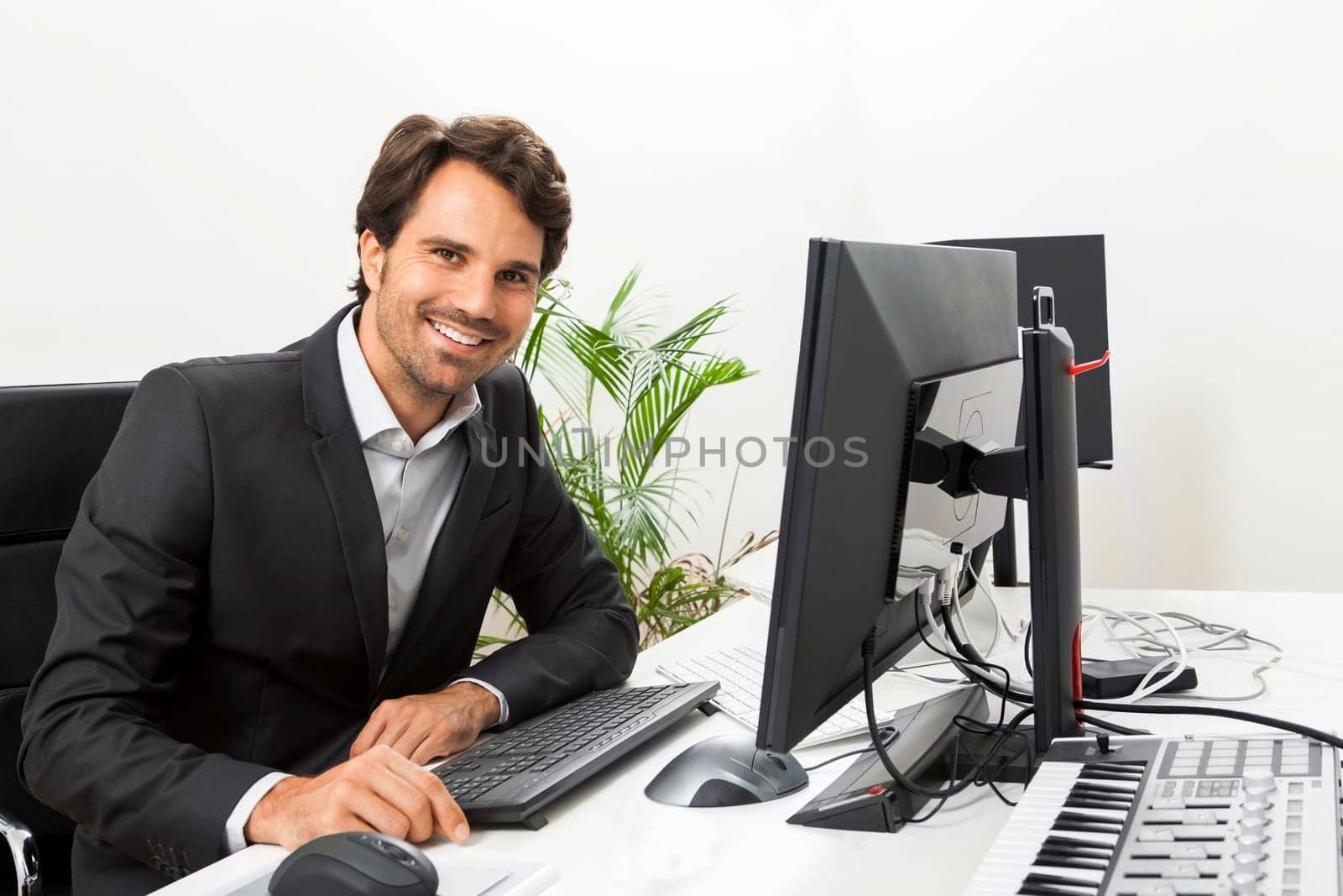 Young successful businessman with black suit in the office at work with computer in concept