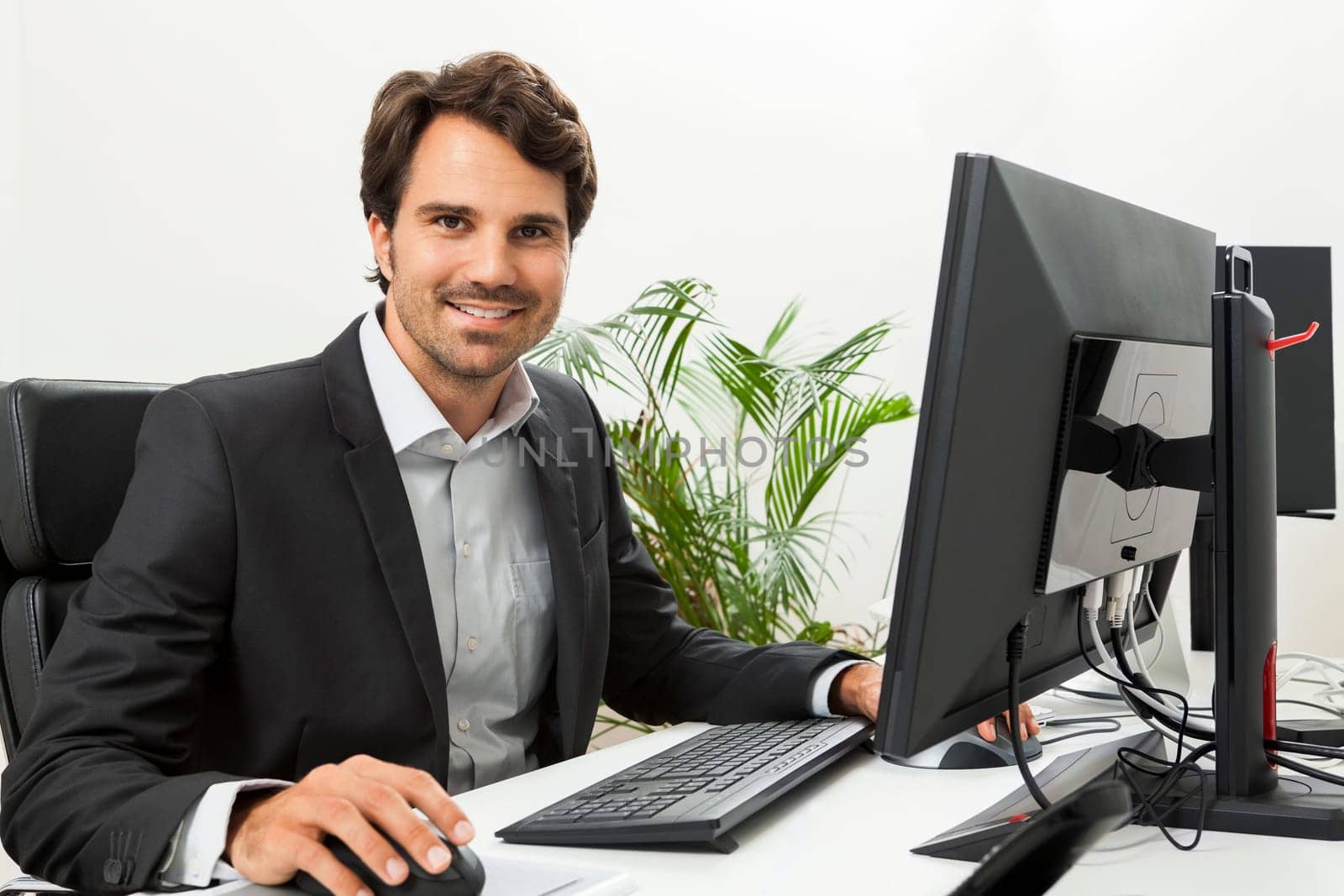 Young successful businessman with black suit in the office at work with computer in concept