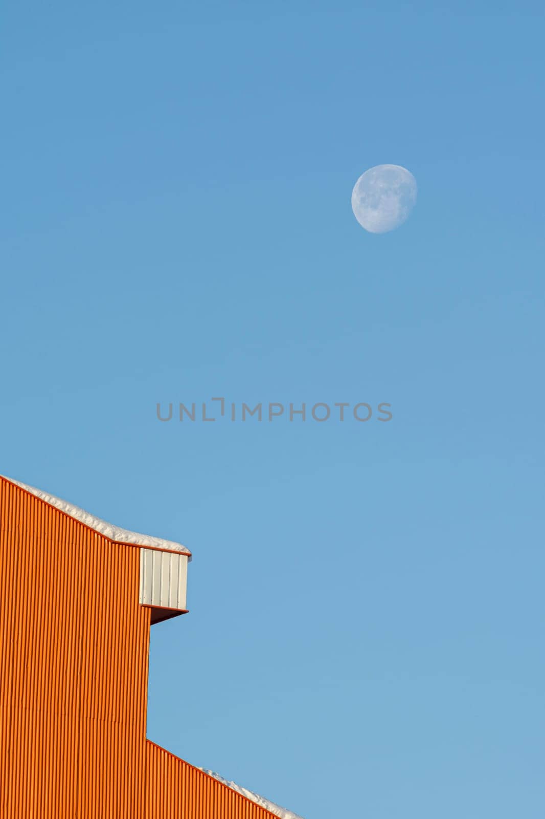Detail shot of a house building rooftop after a snowfall in winter season, morning moon at blue sky- minimal shot
