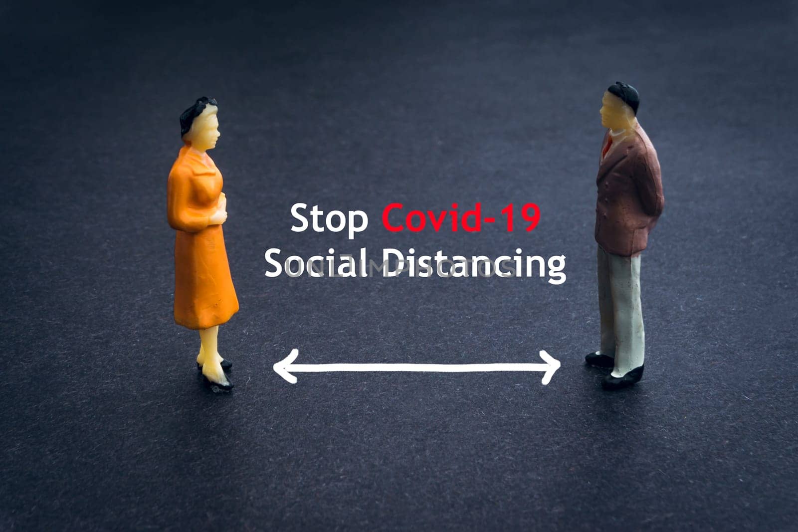 STOP COVID-19 SOCIAL DISTANCING text with miniature people on dark background. Covid-19 or Coronavirus concept
