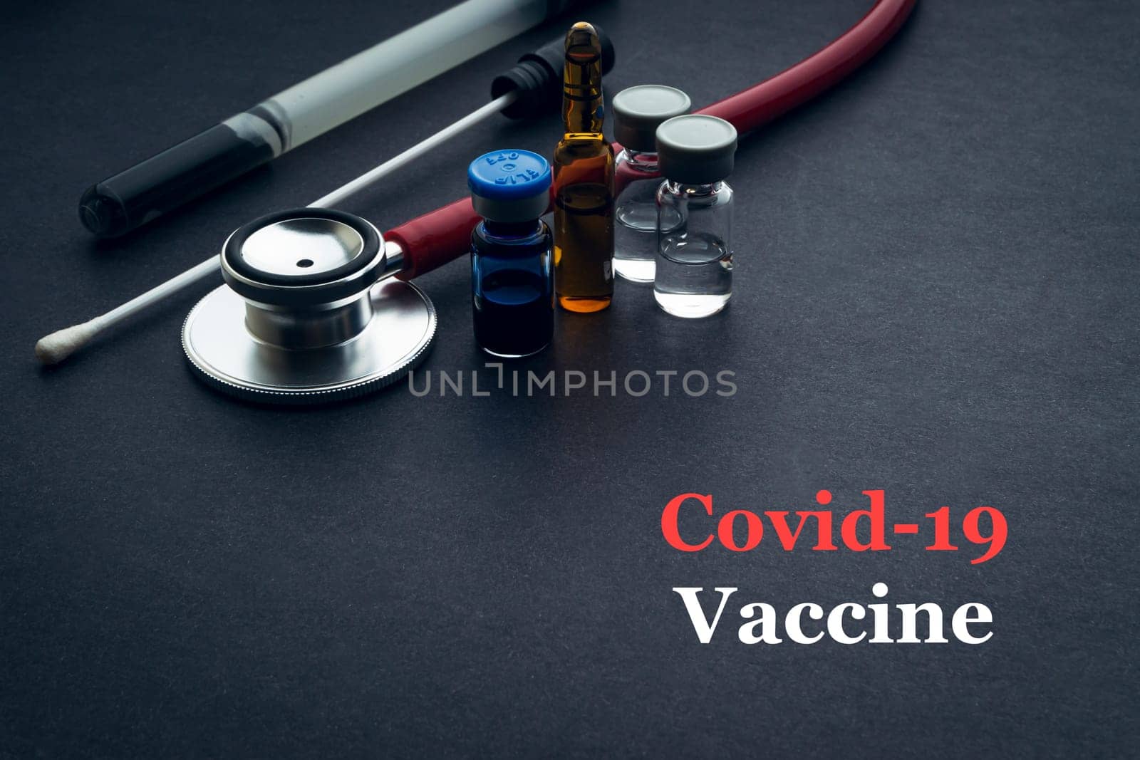 COVID-19 or CORONAVIRUS VACCINE text with stethoscope, medical swab and vial on black background. Covid-19 or Coronavirus concept.