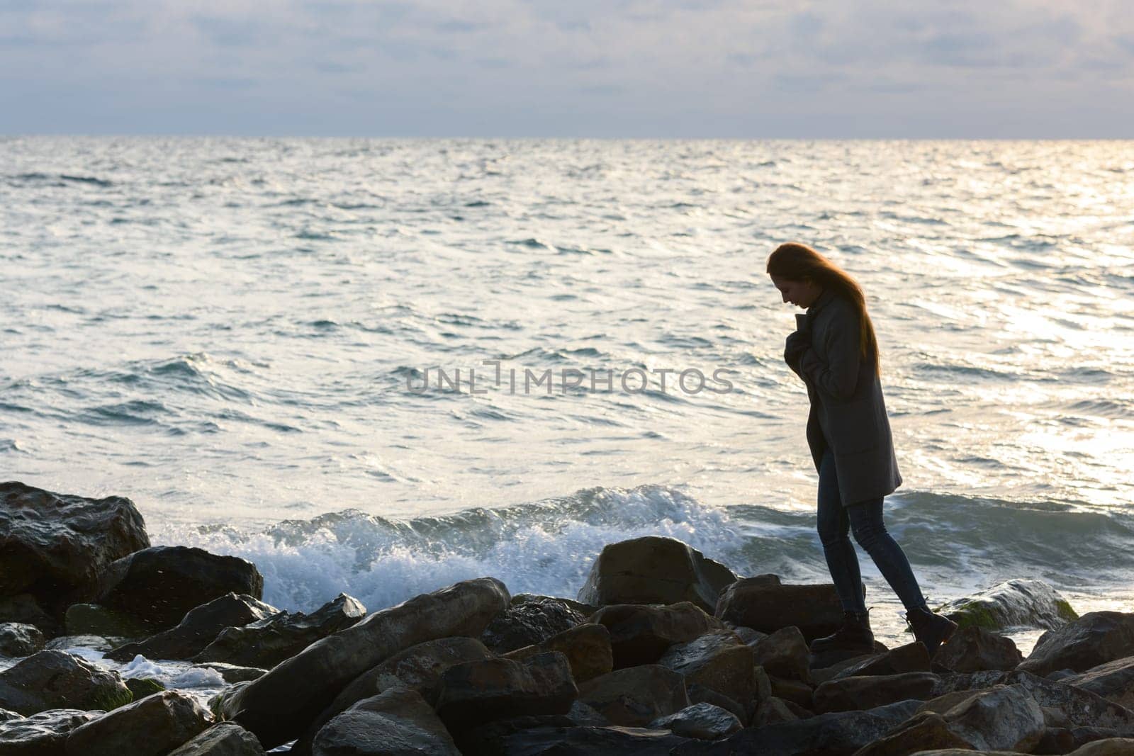 Lonely girl in a depressed mood walking along a rocky seashore