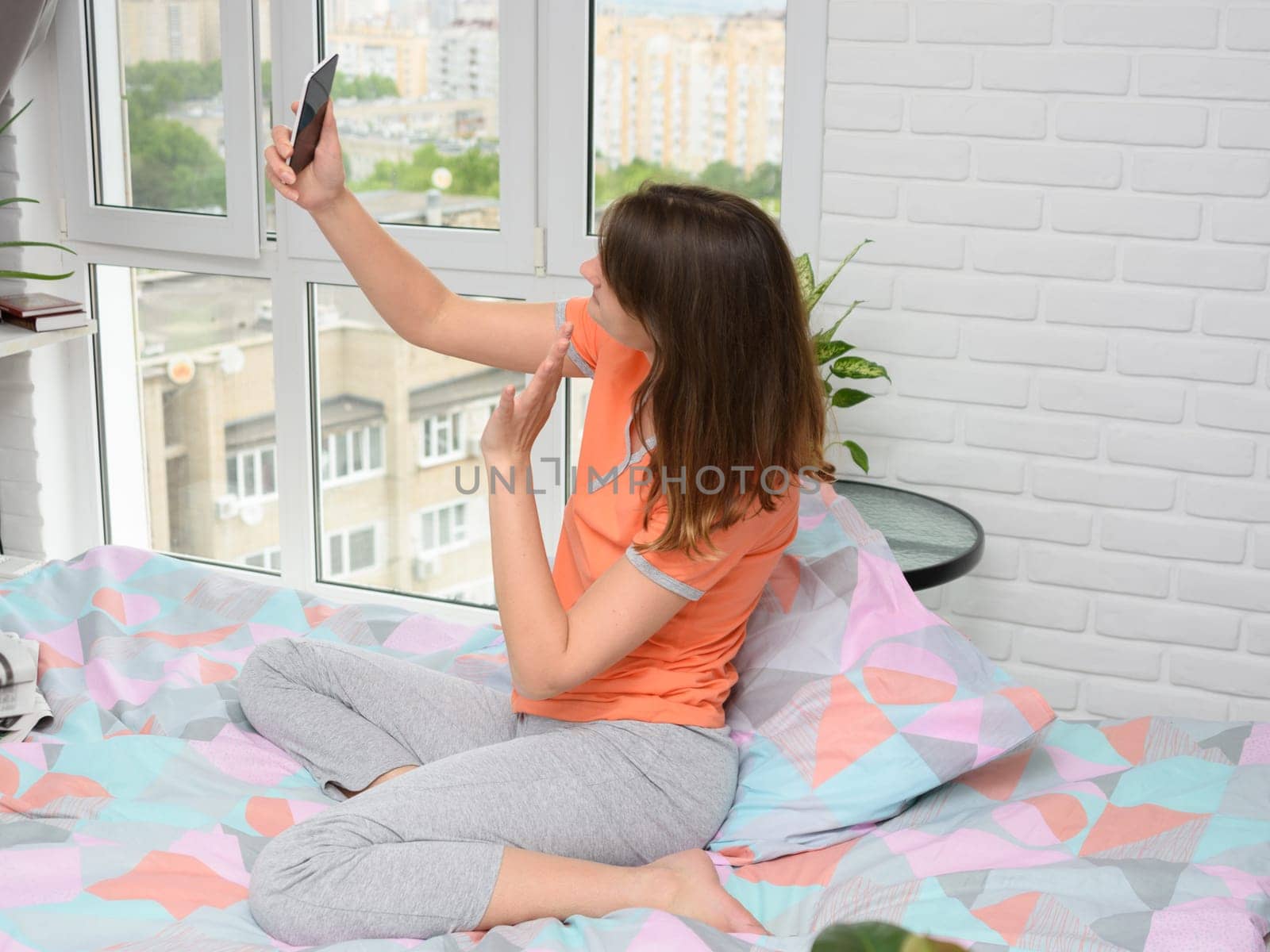 Girl sitting on bed at home happily communicates with her friend via video calling