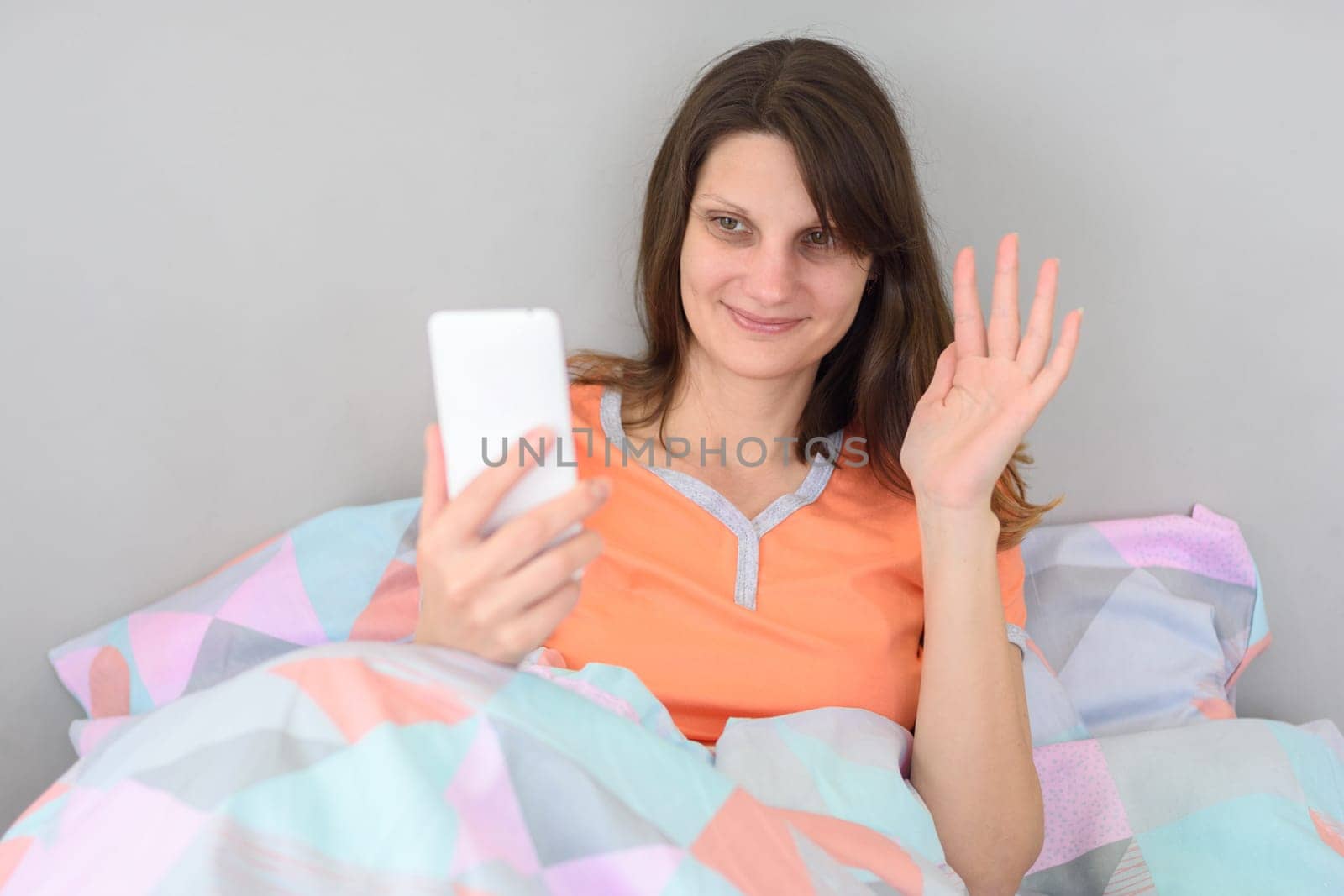 Girl lying in bed waving her hand while chatting via video calling
