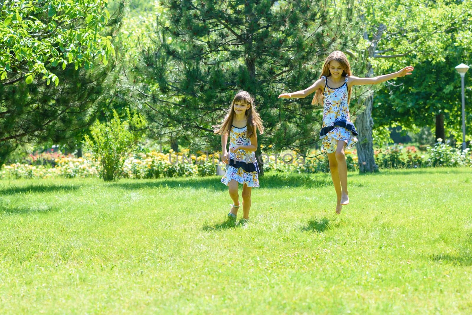 Two girls have fun running on the green lawn in the park