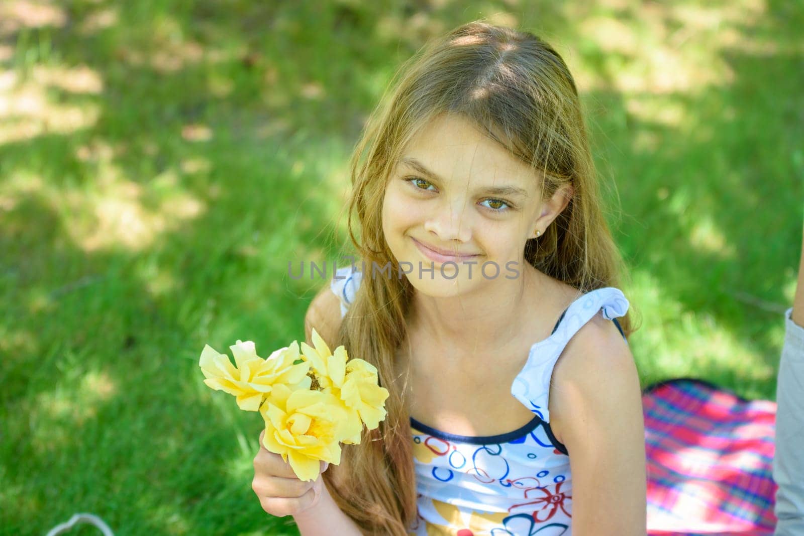 A tousled girl sits in a clearing and holds a bouquet of yellow roses