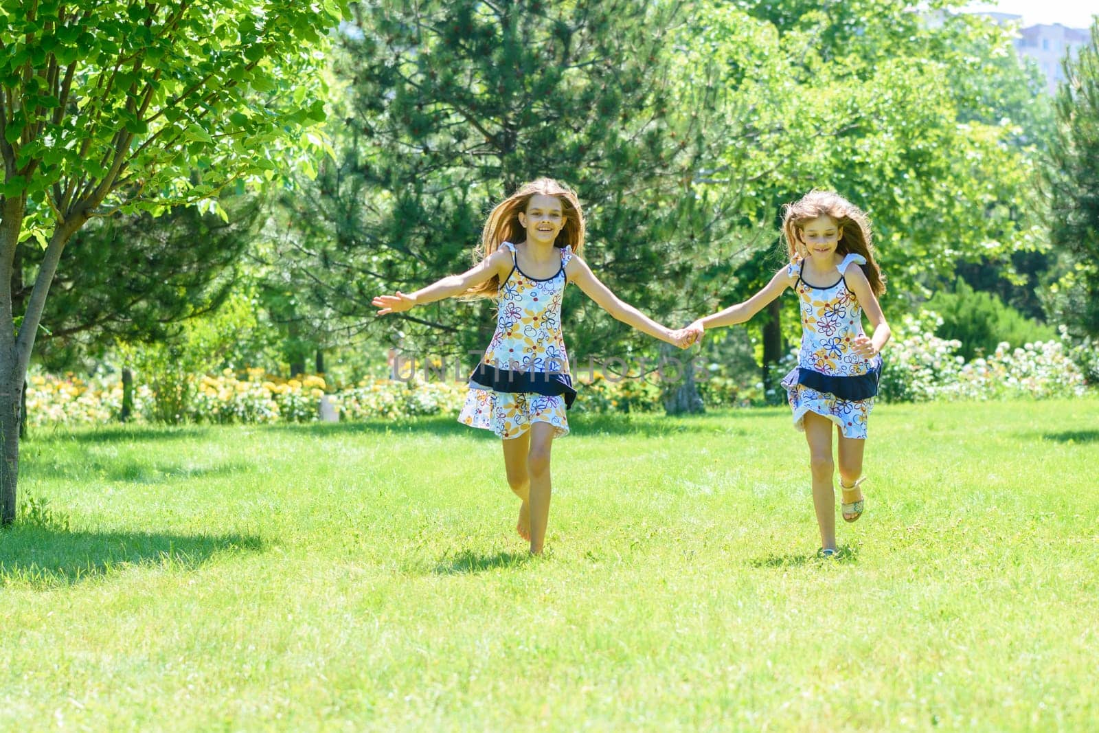 Two girls holding hands run on a green lawn in a park