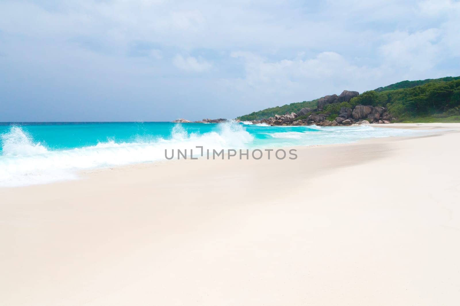 White sand beach with some waves and blue sky in the far a hill with green plants