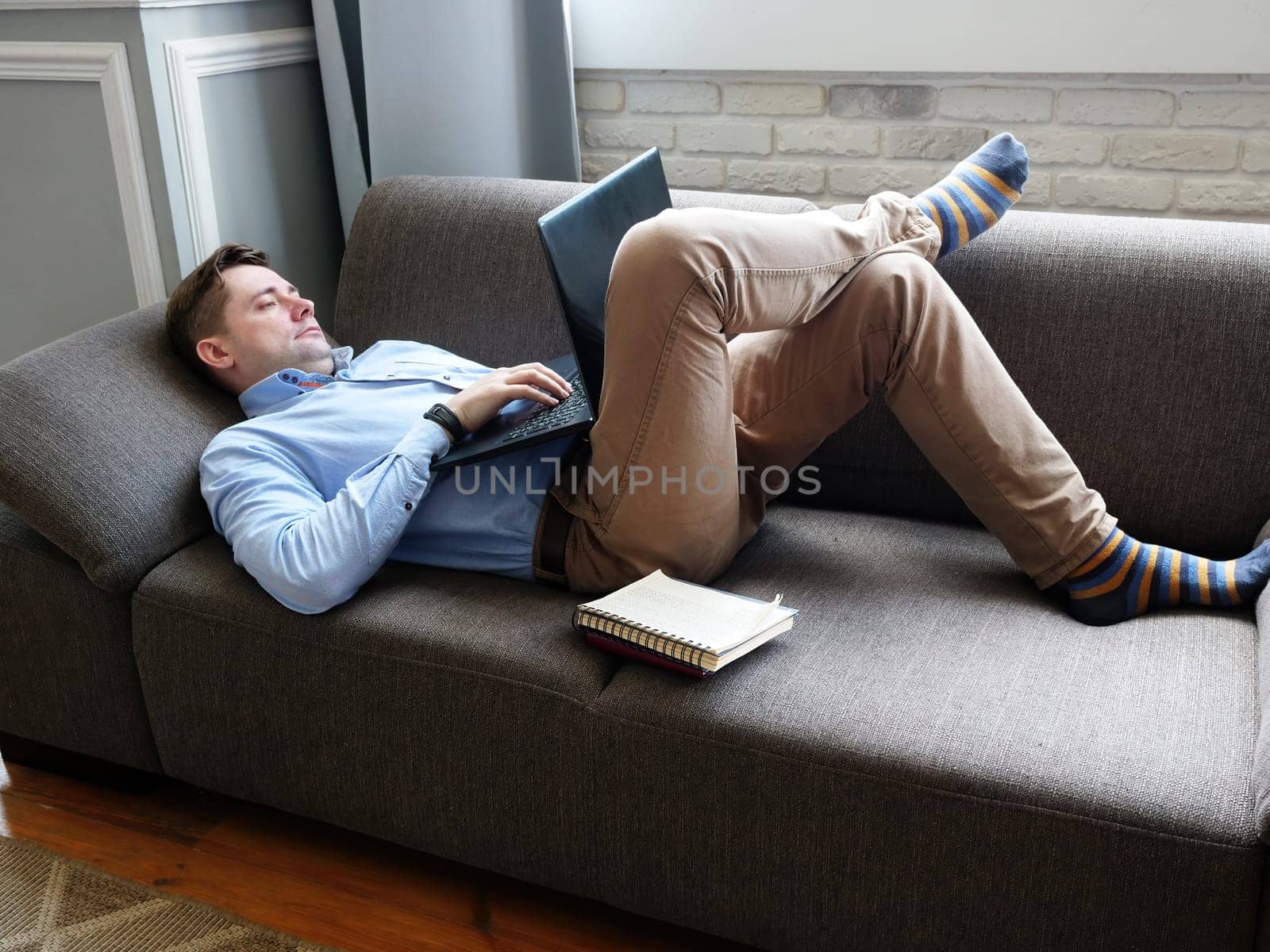 A man lies at home on the couch and works on a laptop. Remote work concept.