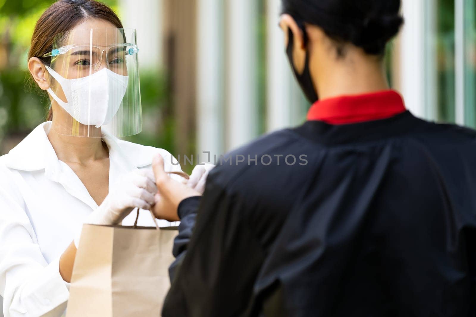 Portrait of atrractive asian woman give bakery grocery bag to delivery man to deliver it to customer make online order. Food delivery service concept in new normal after coronavirus pandemic.