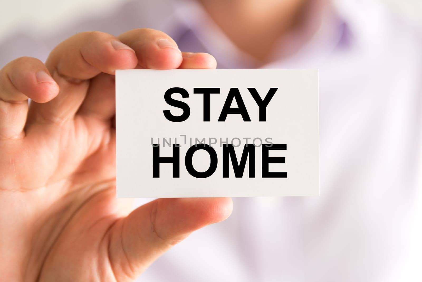 Closeup on businessman holding a card with text Stay Home, business concept image with soft focus background