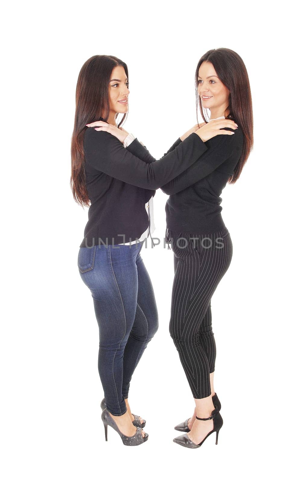 Two beautiful young woman standing face to face in jeans and heels.looking at each other, isolated for white background.