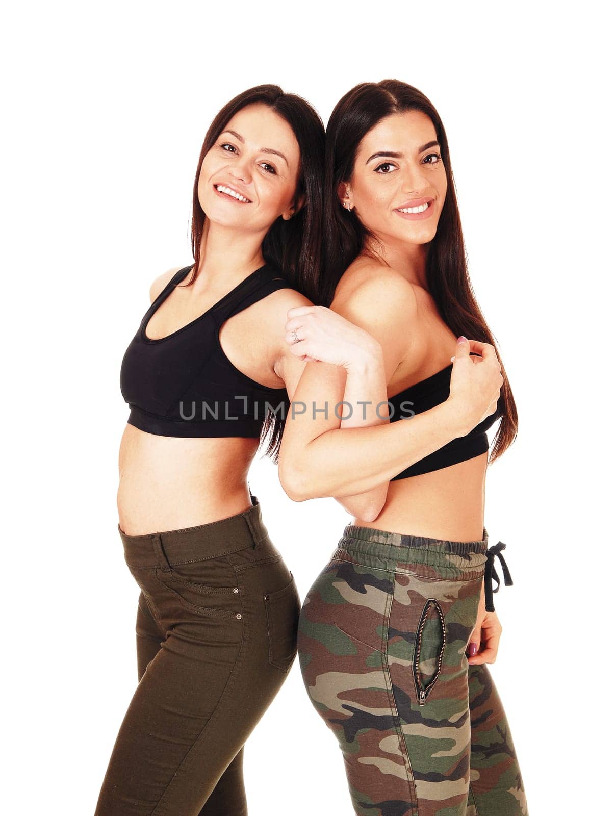 Two beautiful young woman standing back to back in jeans,.smiling and looking at the camera, isolated for white background.