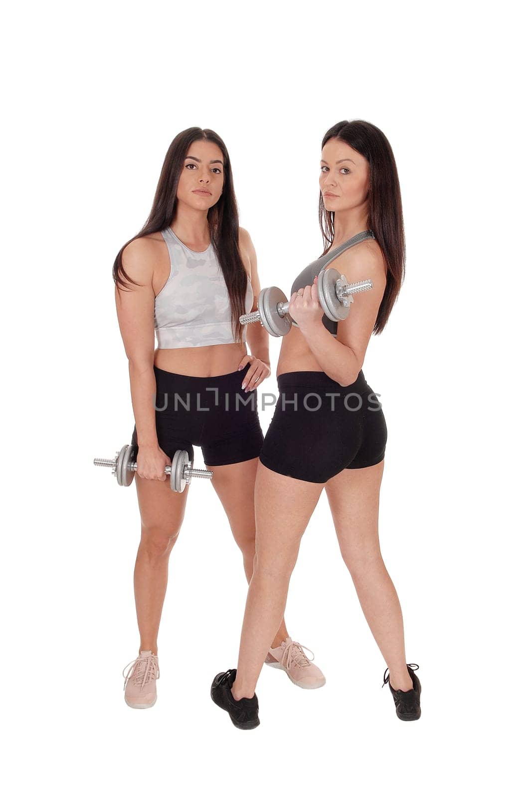 Two beautiful young woman standing in workout outfits in the studio.working out with there dumbbells, isolated for white background.