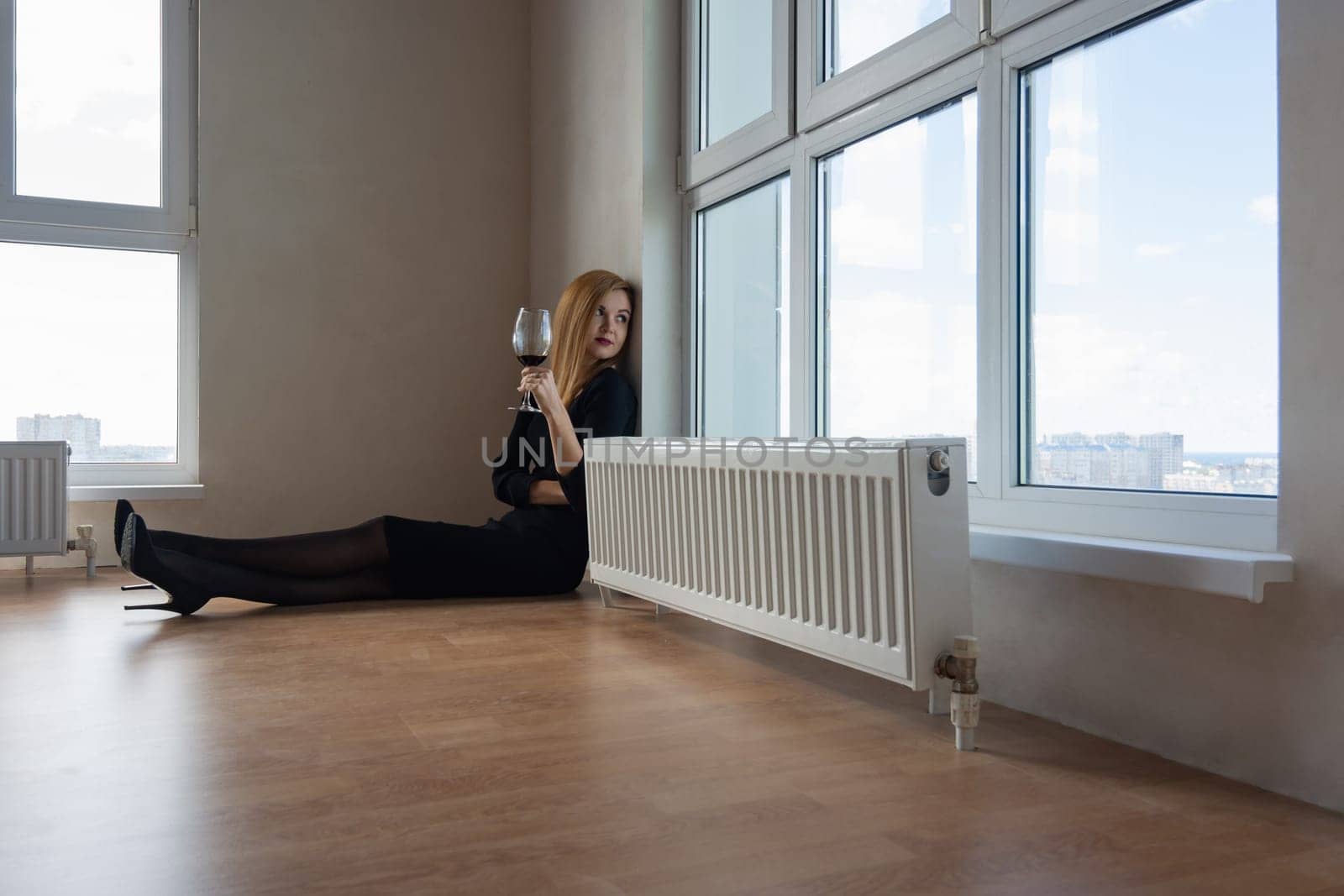 girl thoughtfully stares into a large window with a glass of wine in her hand