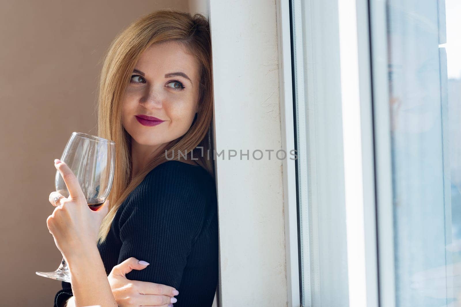 portrait of a girl with a smile looking out the window with a glass of wine