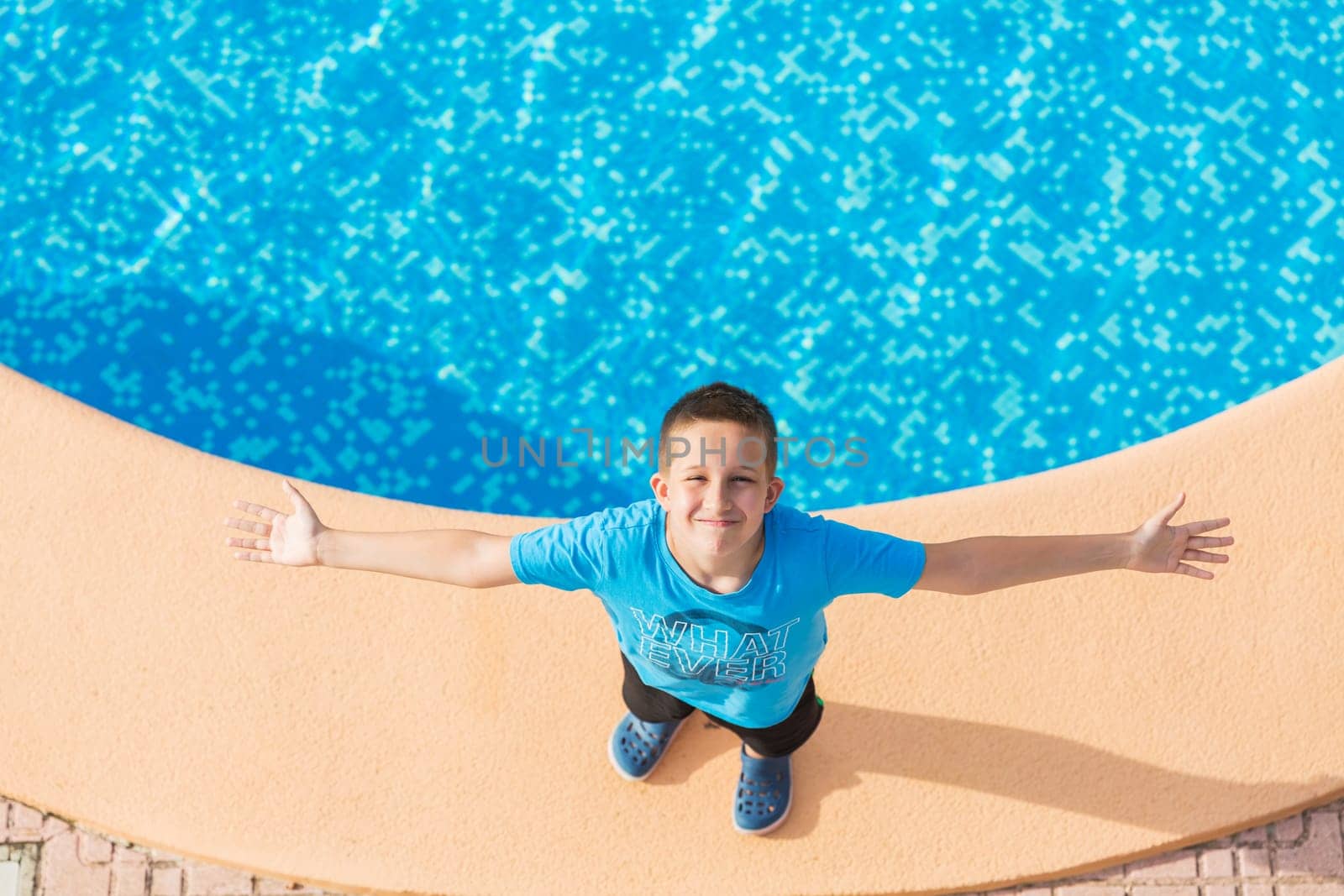 Boy standing at the swimming pool and enjoying the holiday - top view