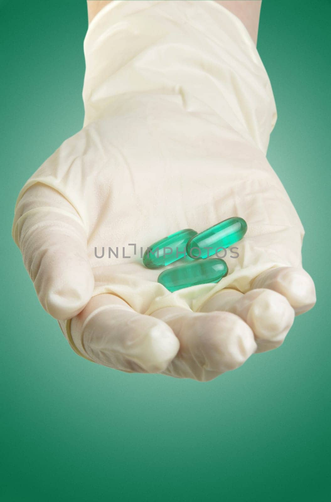 hand with medical gloves and pills on green surface