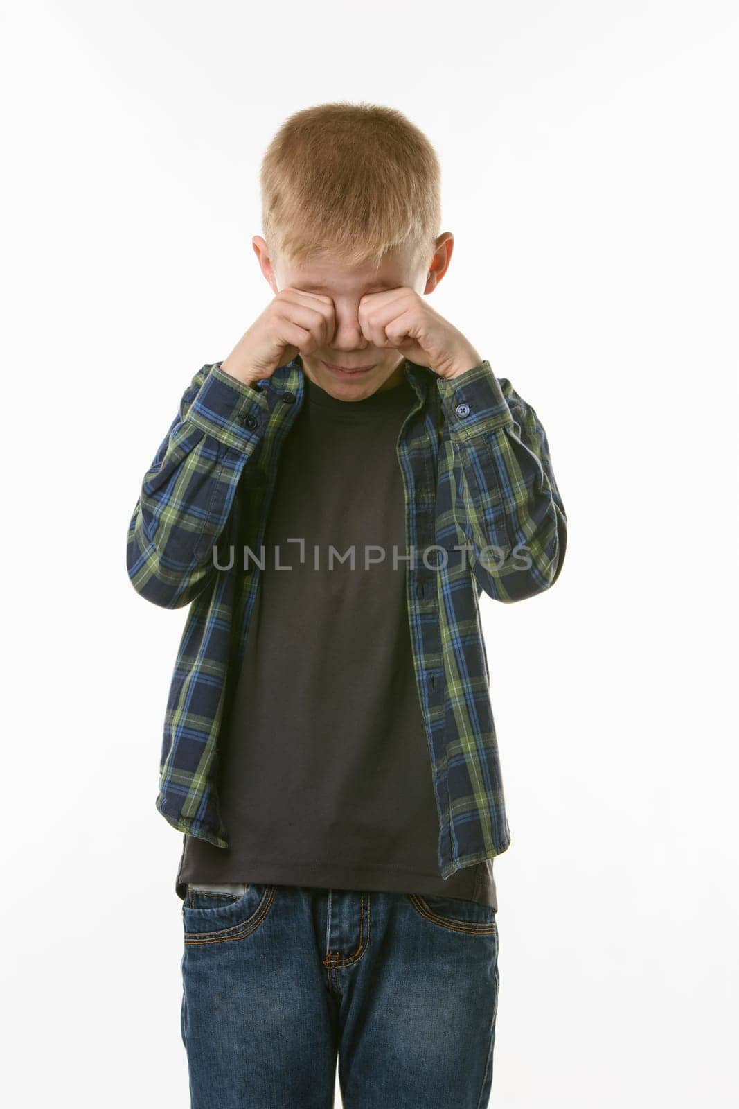 Crying boy rubs his eyes with his fists