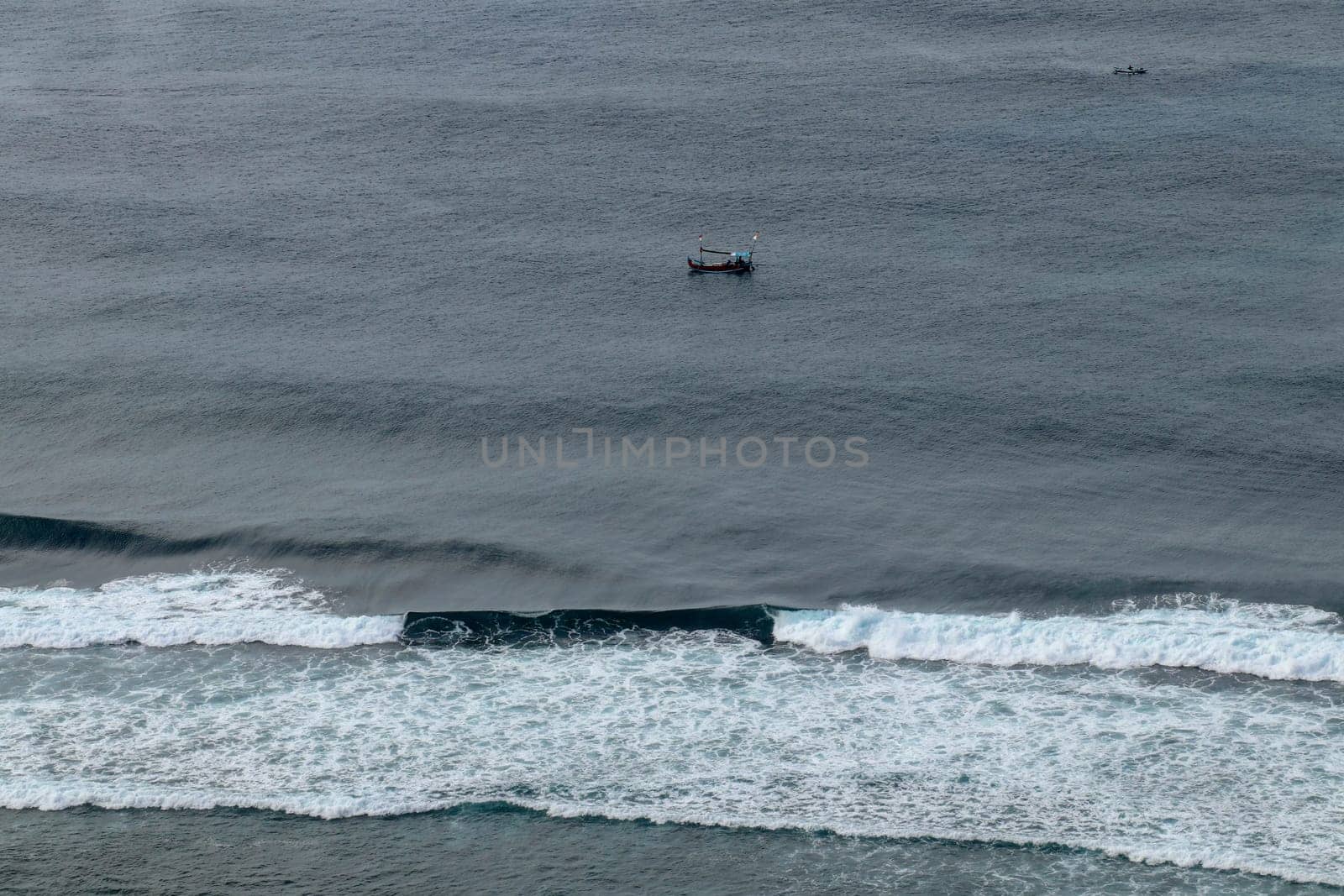 Aerial view of Nyang Nyang beach on Bali in Indonesia. A popular spot of surfers with big waves in the Indian Ocean. Fishing boats of Balinese fishermen on the sea surface. Waves break off the coast.