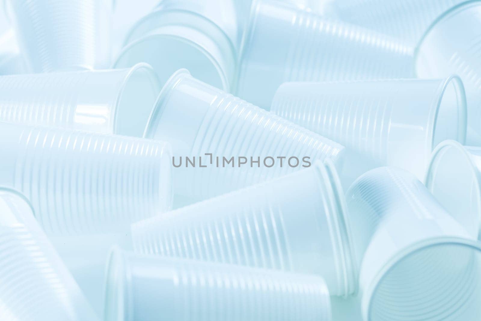 Disposable white plastic cups as background. Environmental concept. Non-compostable waste. In blue tone.