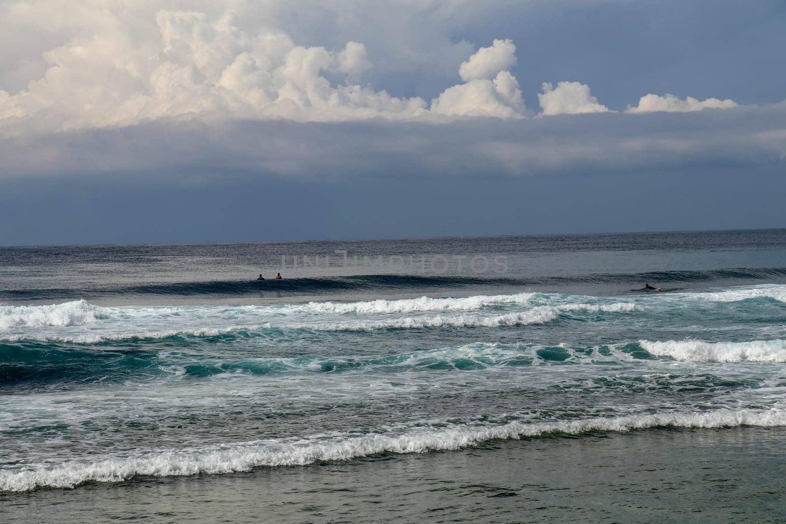 Surfers are waiting for a convenient wave on their surfboards. Tropical surfers paradise with Nyang Nyang beach on Bali island. Azure blue sky, sunny day. Wild waves are approaching the shore in rows.