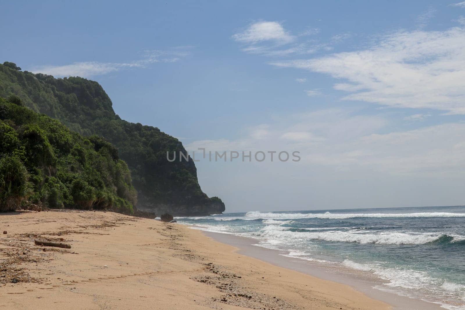 Virgin beach with fine yellow sand on Bali island. Tropical paradise with Nyang Nyang beach with high cliff on background. Wild waves are approaching the shore in rows. Sea foam in rolling waves.