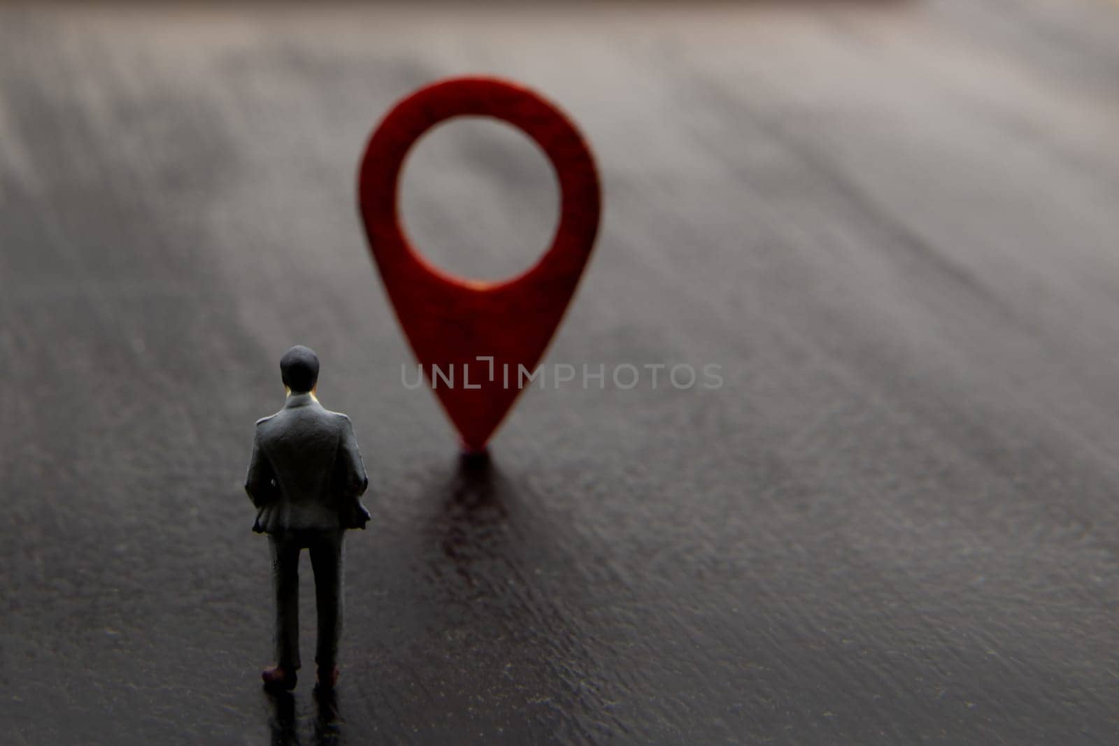 Miniature figurine posed as standing visualising businessman making decision on direction to reach destination marked by red navigation icon, minimalist concept image with copy space on the right
