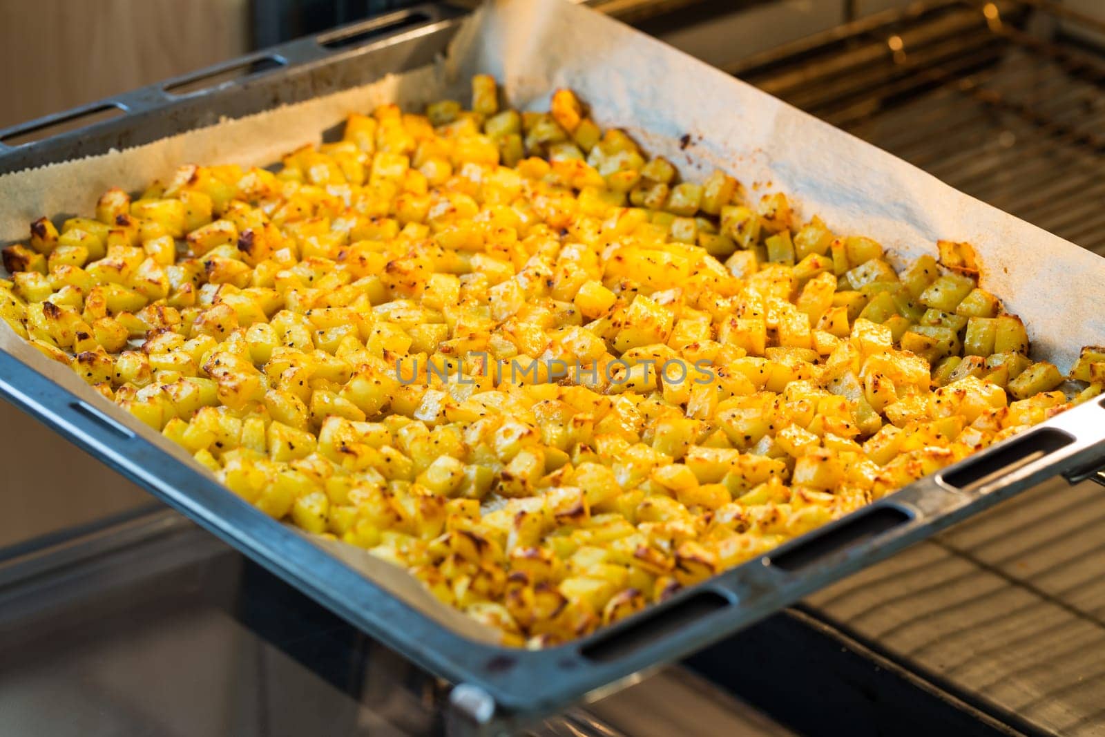 Baking tray with golden roasted potatoes in the open oven