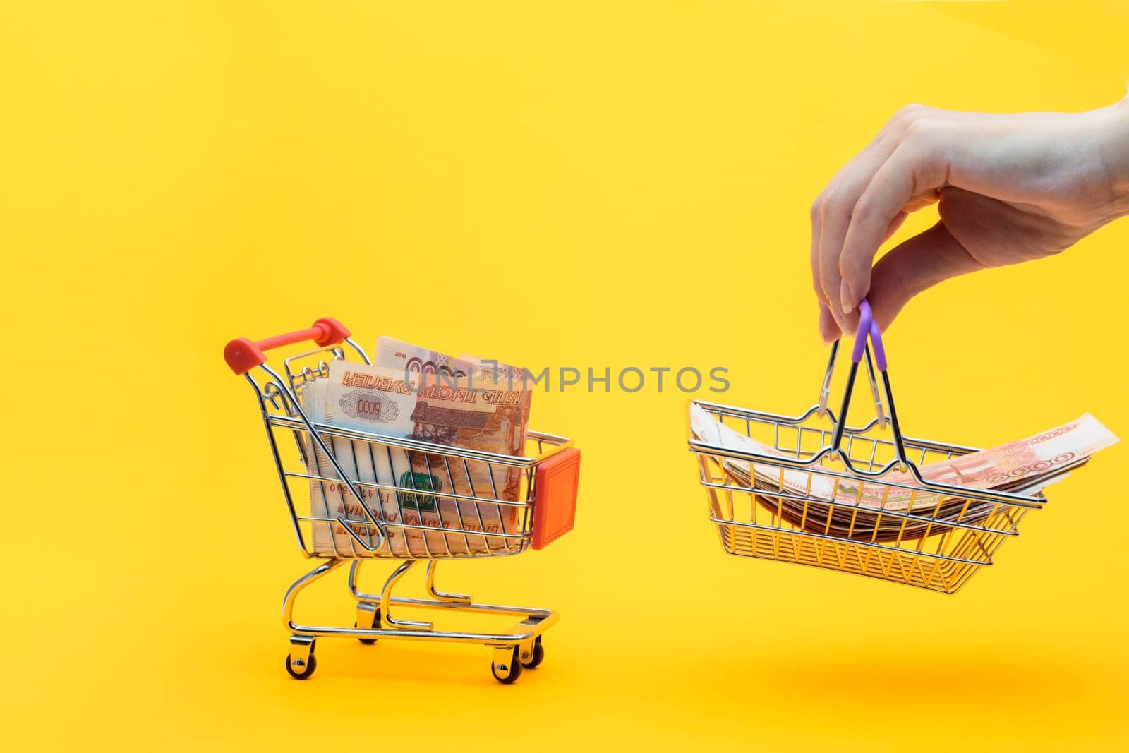 Five thousandth bills are in the grocery cart, a hand holds a grocery basket with bills