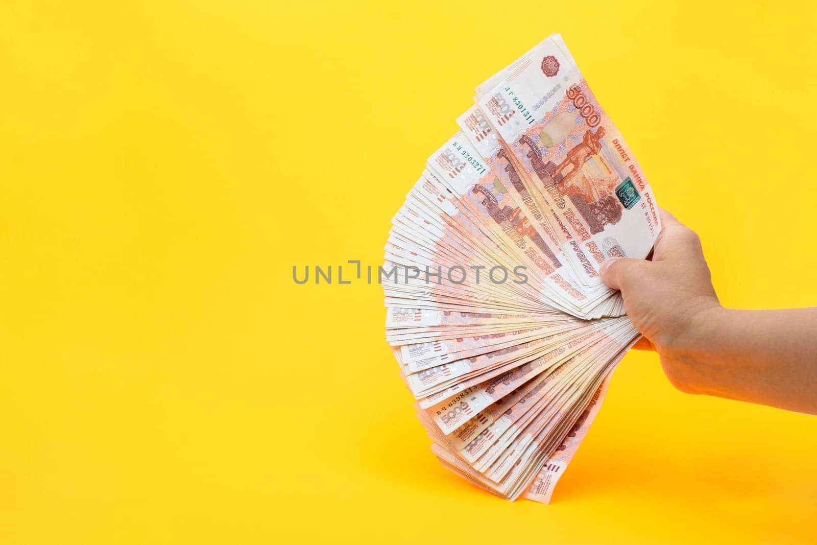 Hand holds a fan from a pack of five thousandth Russian bills on a yellow background