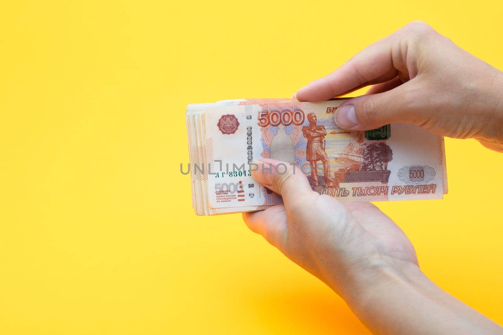 Two hands holding a crustacean of five thousandth Russian rubles on a yellow background