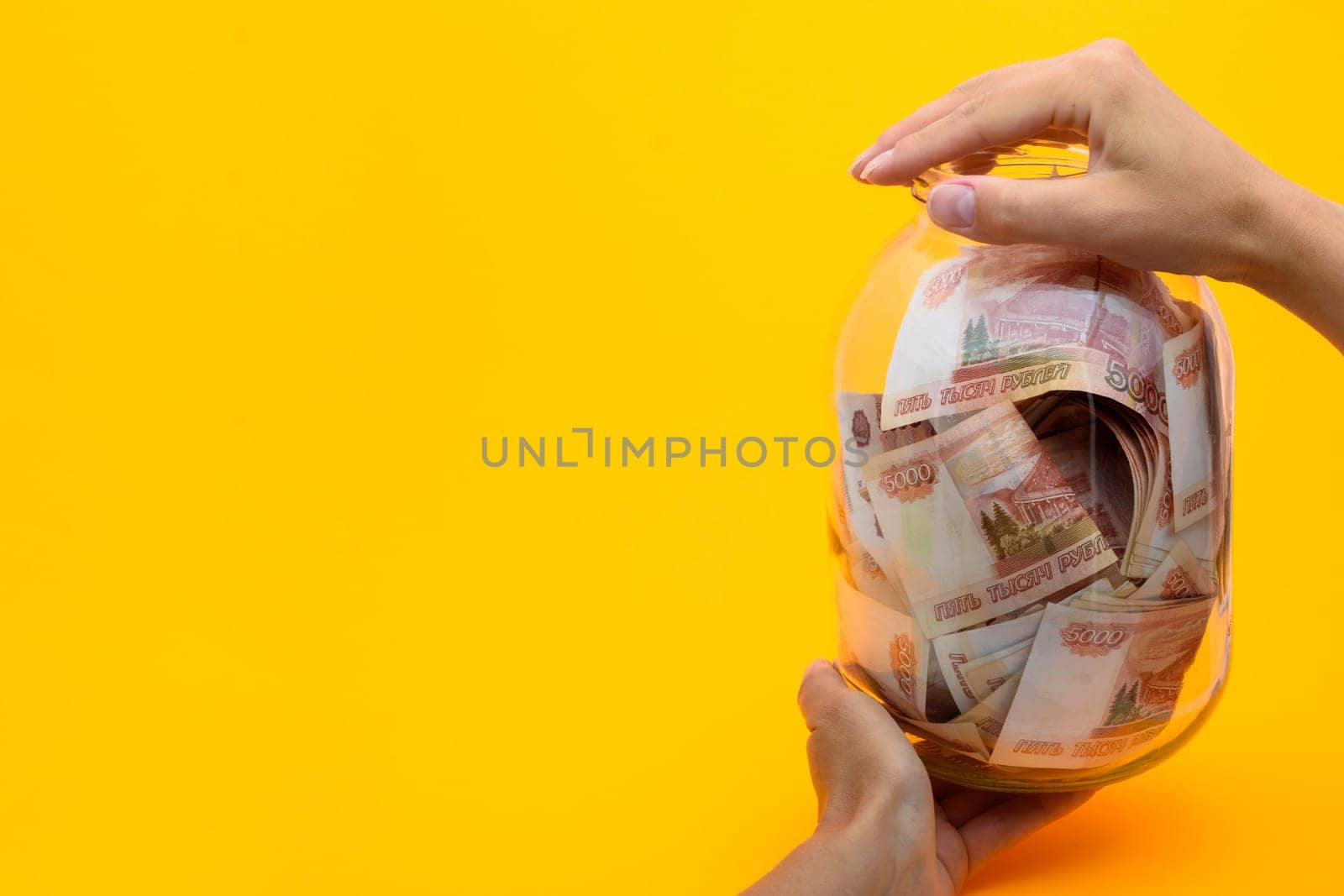 Hands holding a three-liter jar in which lie five thousandth bills