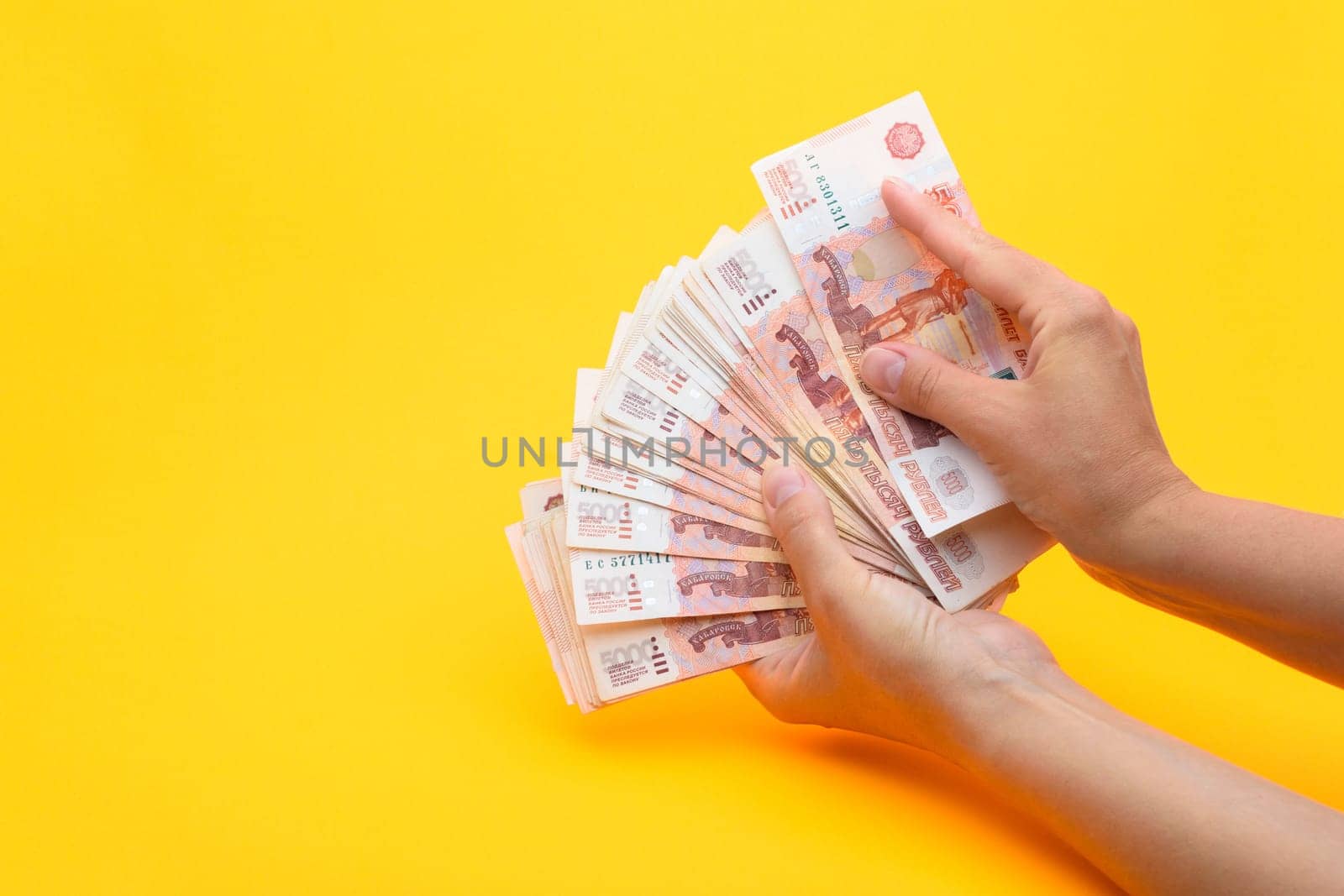 Hands count money in a bundle of notes, yellow background