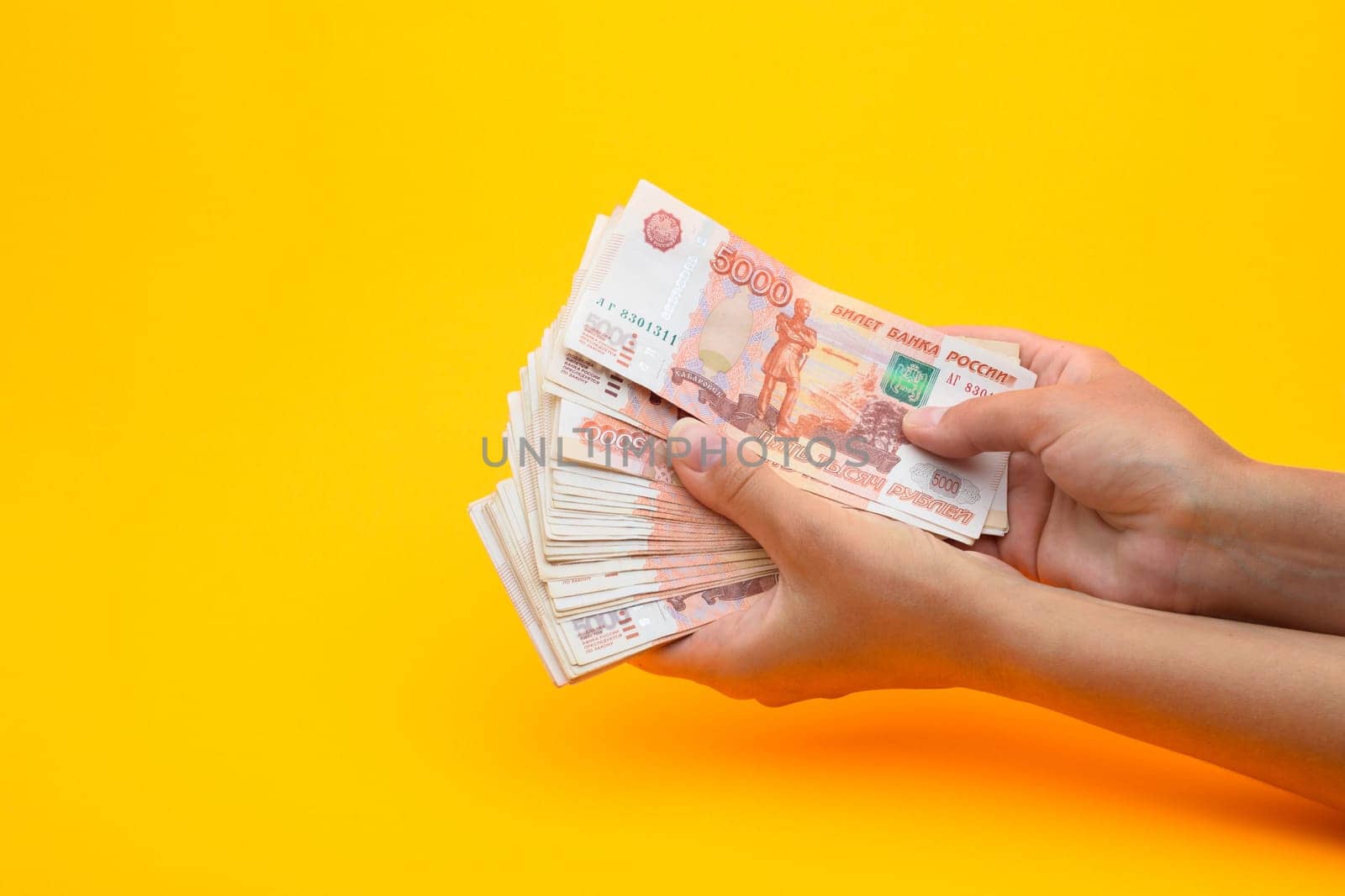 In hands lies a bundle of five thousandth bills on a yellow background