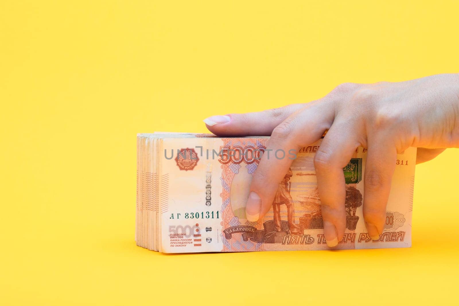 Hand covered a pack of five thousandth bills, yellow background
