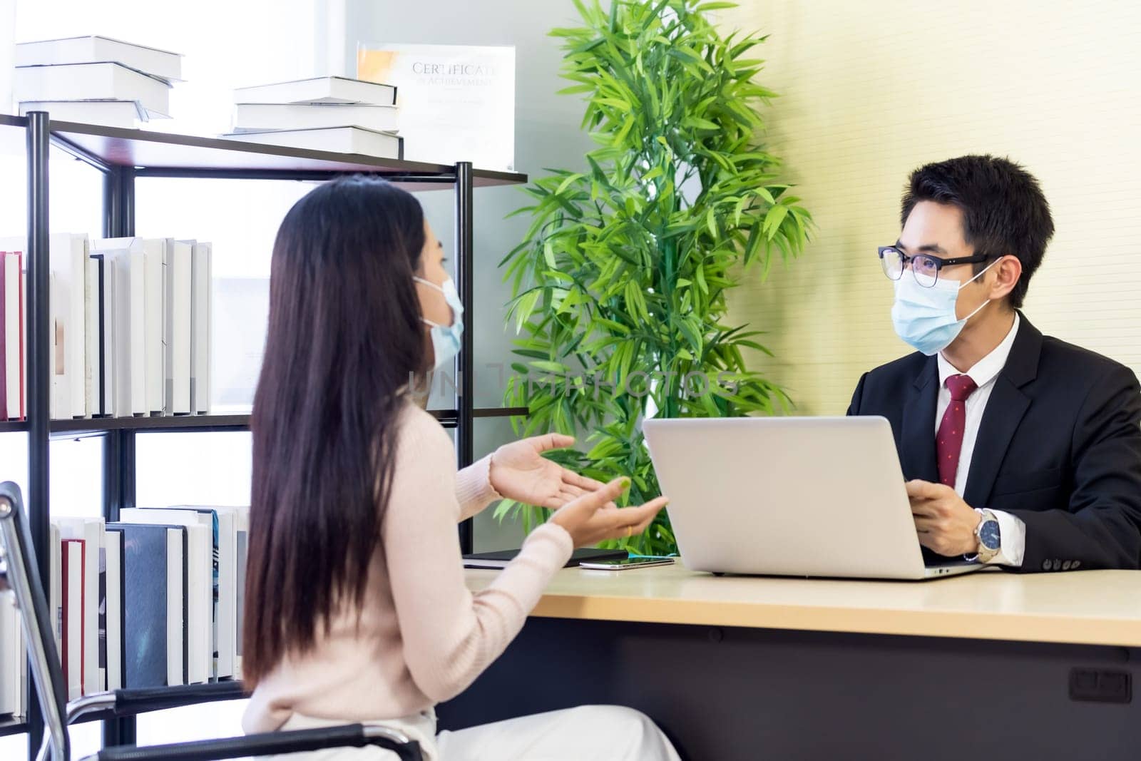 Portrait of asian business advisor giving advice to customer about financial loan situation in bank office. New normal social distance business for banking financial and investment concept.