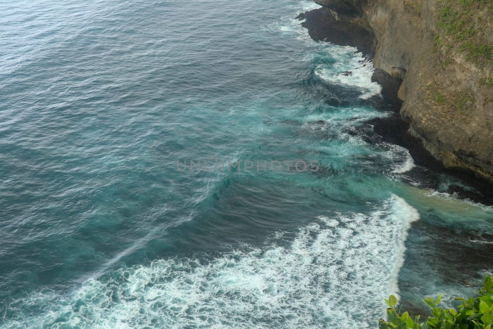 Overview panorama ocean shore, cliff. Sunset. Bali. Overwhelmed scene the flower and green-capped vertical cliff over the Indian ocean. South of Bali island, Pura Luhur Uluwatu Temple. Indonesia.