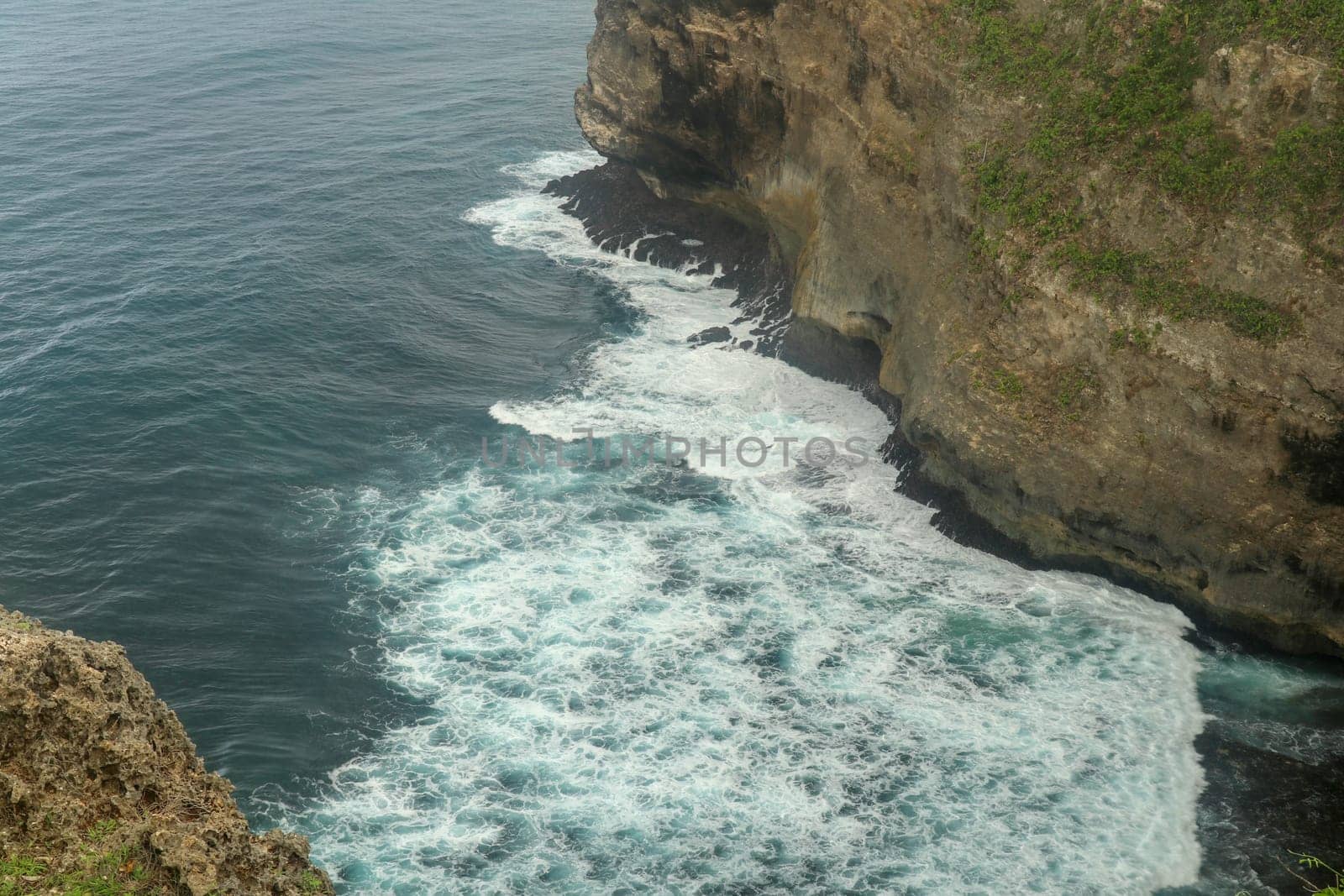 Overview panorama ocean shore, cliff. Sunset. Bali. Overwhelmed scene the flower and green-capped vertical cliff over the Indian ocean. South of Bali island, Pura Luhur Uluwatu Temple. Indonesia.