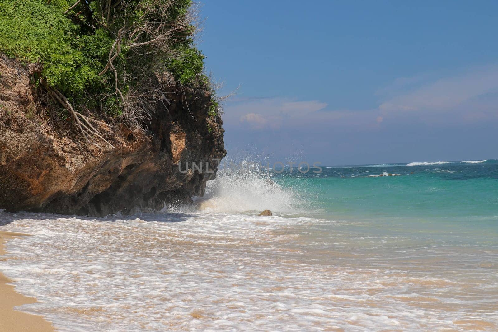 Pantai Gunung Payung beach with fine golden sand, Bali. Turquoise blue water turns into sea foam as the waves break against rocky cliffs of the coast. Sunny day with blue sky. Tourist natural concept.
