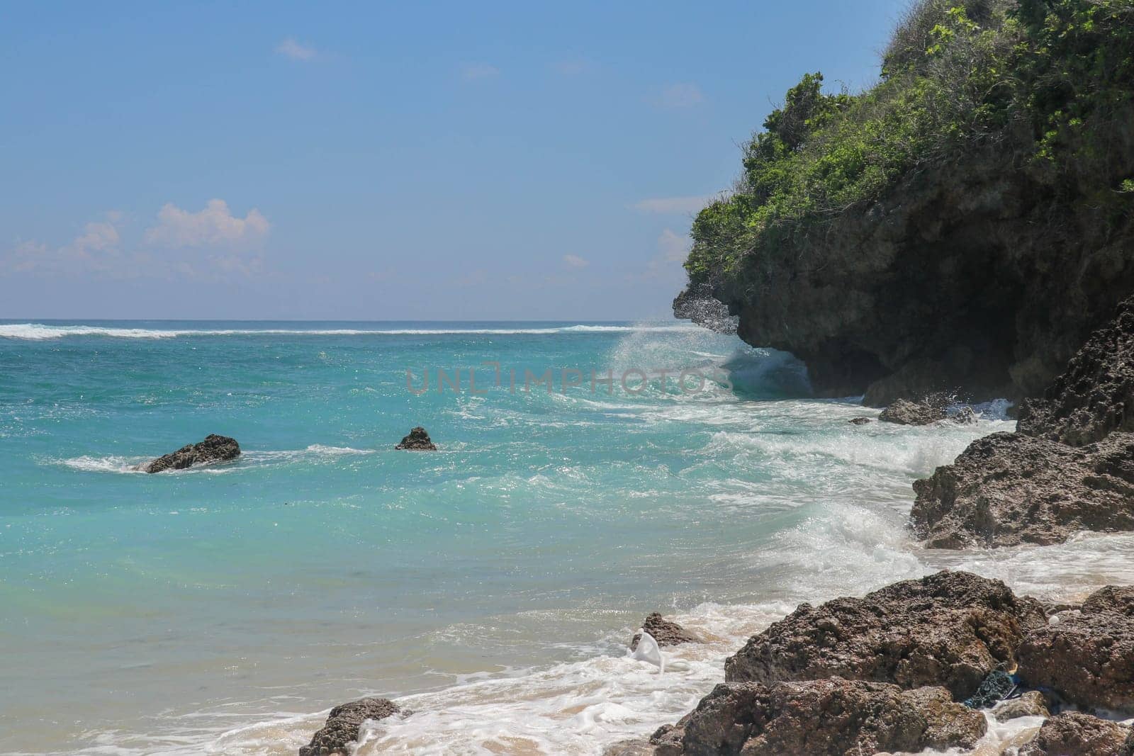 Pantai Gunung Payung beach with fine golden sand, Bali. Turquoise blue water turns into sea foam as the waves break against rocky cliffs of the coast. Sunny day with blue sky. Tourist natural concept.